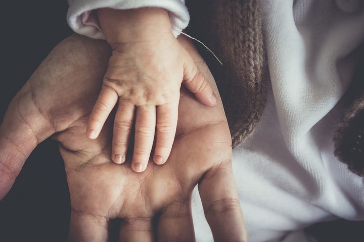 hands of infant on top of adult's hand