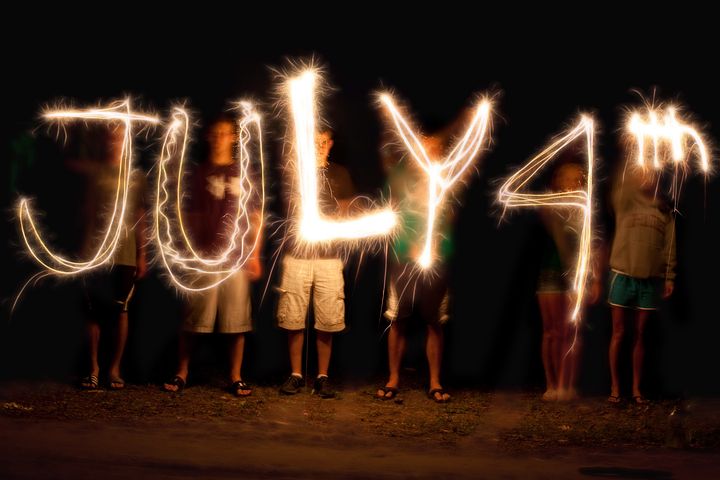 People lined up and using sparkles sticks to write JULY 4th at night