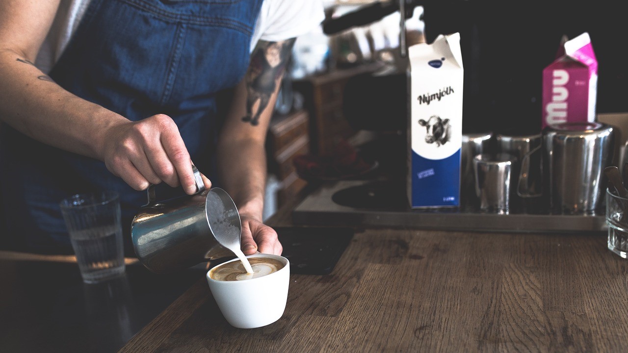 Barista adding milk to coffee cup