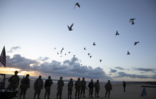 Men in a vintage US WWII uniform watch as pigeons are released during a D-Day 76th anniversary ceremony