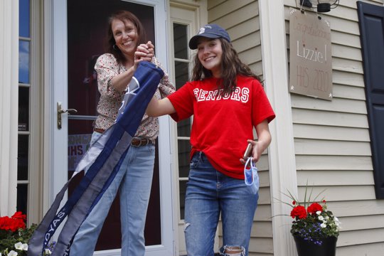 In this June 1, 2020 photo, high school graduate Lizzie Quinlivan and her mom, Julie, hold a Georgetown University windsock at their home in Hingham, Mass. Quinlivan has opted to attend closer-to-home Georgetown instead of colleges on the west coast which were on her original wish-list. As students make college plans for this fall, some U.S. universities are seeing surging interest from in-state students looking to stay closer to home amid the coronavirus pandemic.