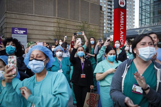 In this April 28, 2020, file photo Medical personnel attend a daily 7 p.m. applause in their honor, during the coronavirus pandemic outside NYU Langone Medical Center in the Manhattan borough of New York. Essential workers are lauded for their service and hailed as everyday heroes. But in most states nurses, first responders and frontline workers who get COVID-19 on the job have no guarantee they'll qualify for workers' comp to cover lost wages and medical care.