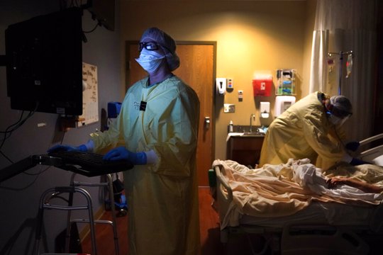 Registered nurse Shelly Girardin, left, is illuminated by the glow of a computer monitor as Dr. Shane Wilson examines COVID-19 patient Neva Azinger inside Scotland County Hospital in Memphis, Mo.
