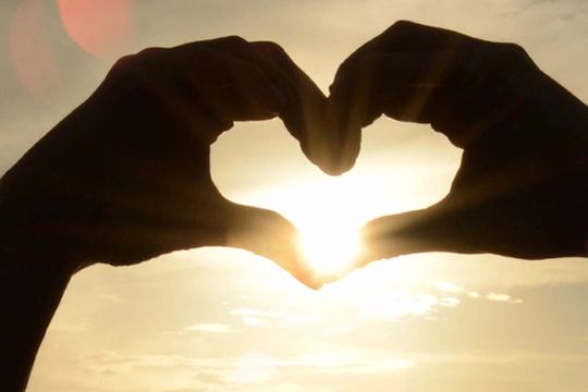 Hands forming heart shape, sunset in background