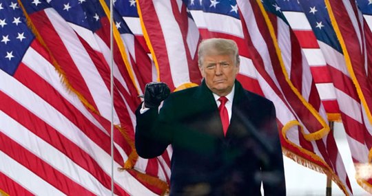 Trump behind a plexiglass and American flags behind him