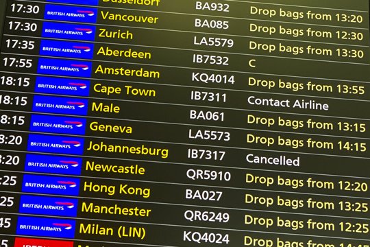 A departures screen displays a cancelled flight to Johannesburg and a message to contact the airline for a scheduled flight to Capetown, at London's Heathrow Airport
