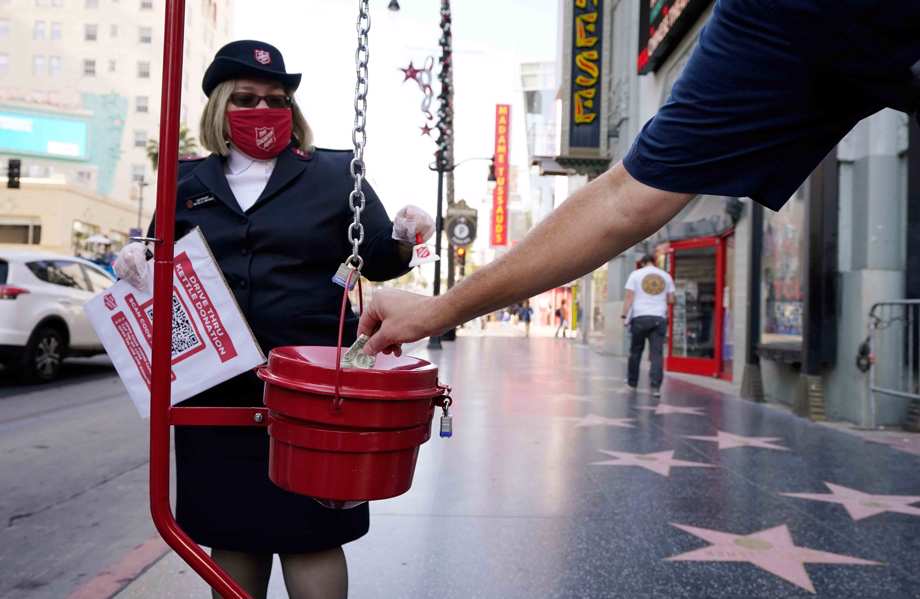  A pedestrian drops a dollar into a collection basket as Michelle Miranda of The Salvation Army looks on during the charitable organization's drive-through donations event at the TCL Chinese Theatre, Thursday, Dec. 10, 2020, in Los Angeles.