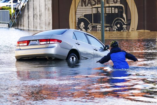 Kenneth Warner races into the water to help rescue the driver of a car that went into the flooded Nooksack River, Tuesday, Nov. 16, 2021, in Ferndale, Wash. Winter has started out weird in the United States. It's been flip flop weather in much of the country with the Pacific Northwest getting record rainfall and Denver and the Rockies still haven't seen their first significant snowfall of the season.