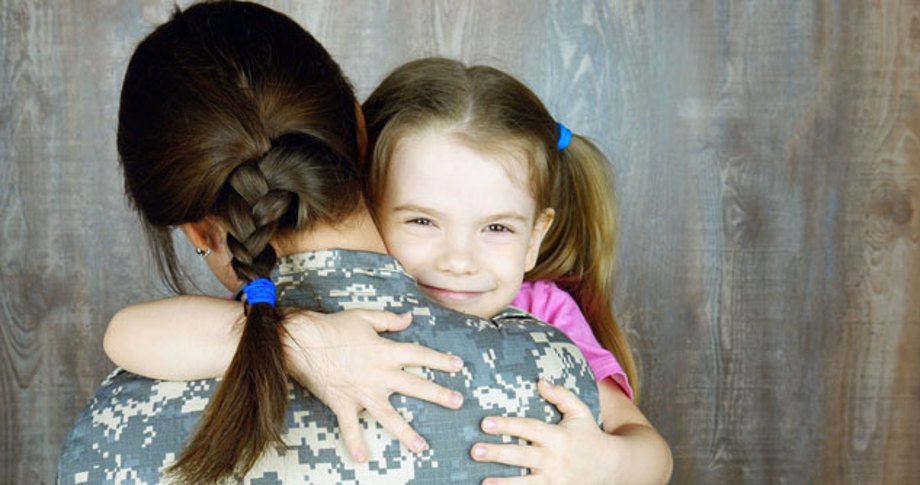 Little girl hugs her military mom, smiles in to camera