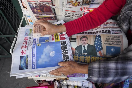 Business owner "Annie" weights down copies of the Chinese Daily News newspaper showcasing pictures of a suspected Chinese spy balloon, in the Chinatown district of Los Angeles Sunday, Feb. 5, 2023