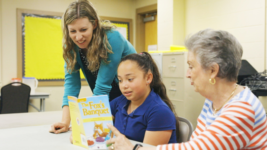 Students, teacher and church volunteer read book