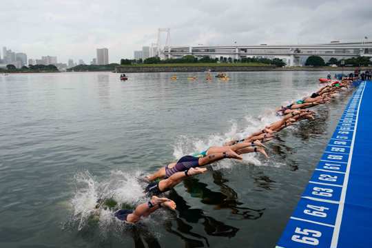 athletes dive into the water at the start line during a women's triathlon test event at Odaiba Marine Park