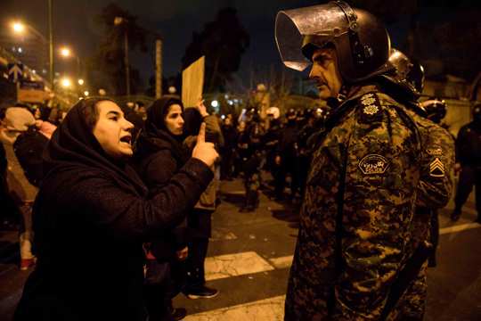 a woman attending a candlelight vigil to remember the victims of the Ukraine plane crash, talks to a policeman, at the gate of Amri Kabir University in Tehran, Iran
