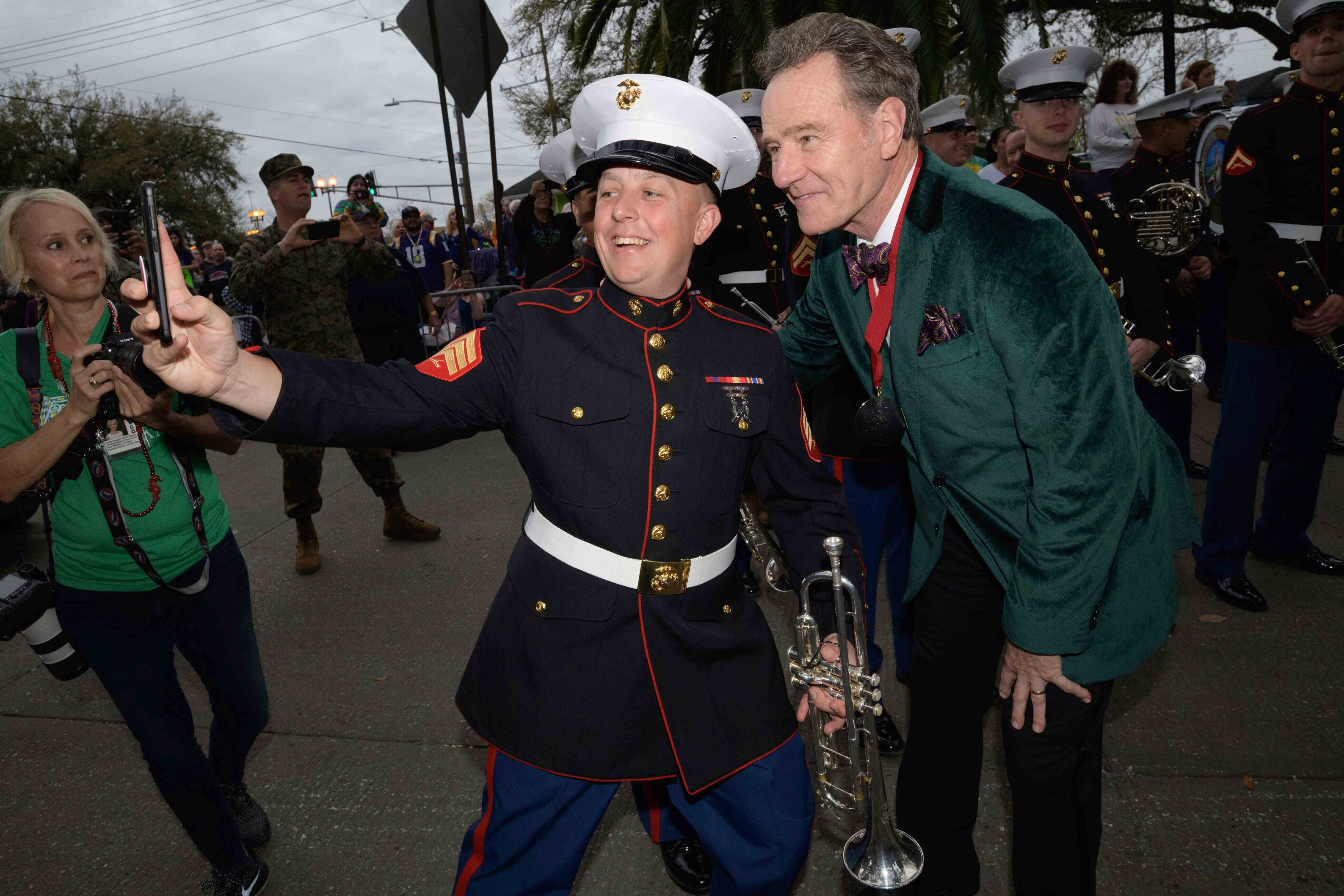 Actor Bryan Cranston takes a picture with a member of the Marine Corps band as he acts as the celebrity monarch of the Krewe of Orpheus along the Uptown parade route during Mardi Gras in New Orleans