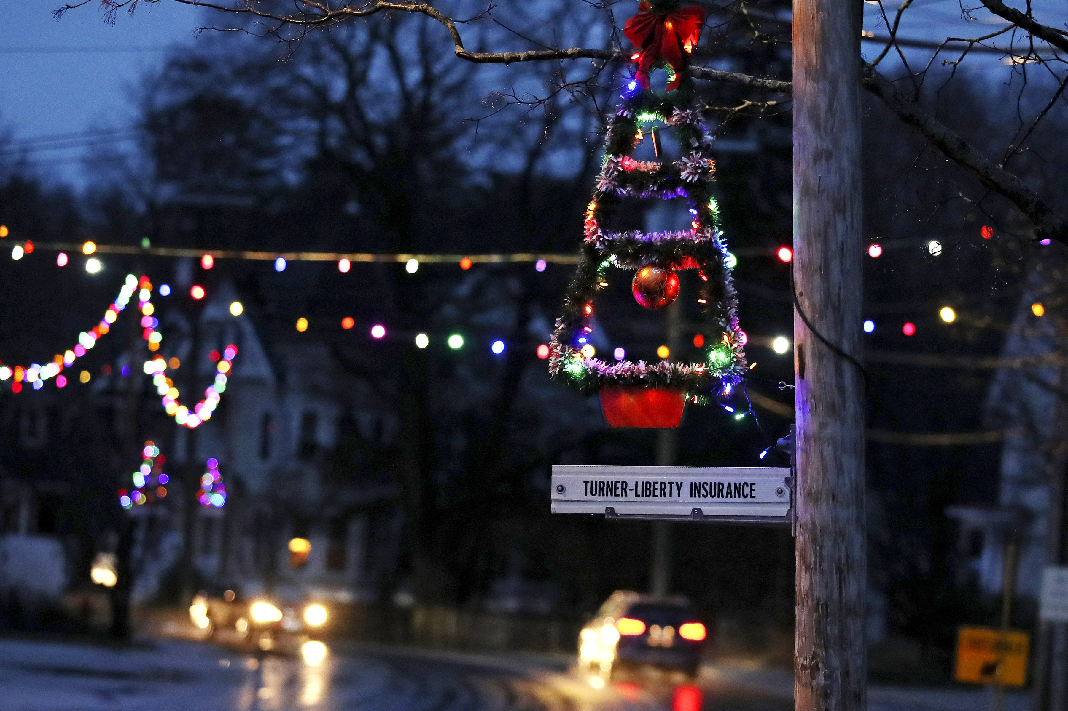 In this March 19, 2020, photo, a lit Christmas tree hangs from a pole at dusk as holiday lights illuminate downtown in Farmington, N.H. As the coronavirus spreads, holiday lights are going back up to provide a bit of emotional and actual brightness.