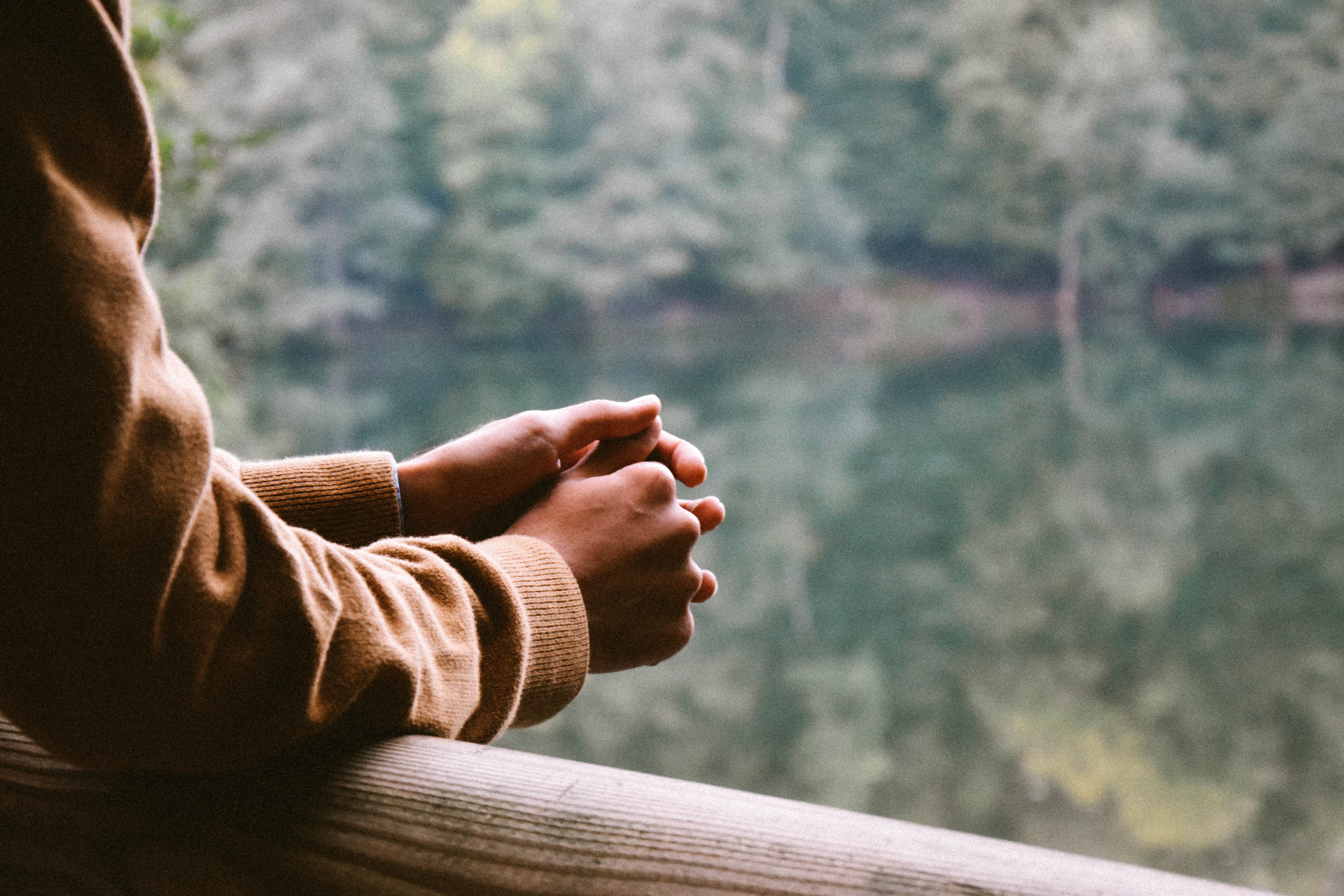 Man in brown coat leans on porch rail, hands clasped