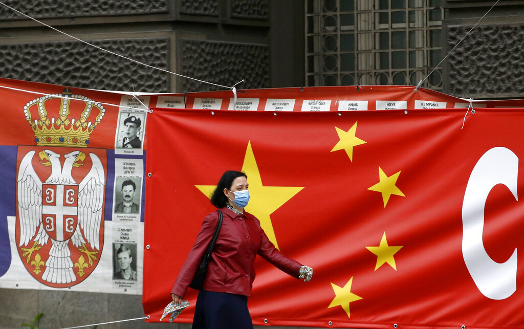 Woman wearing a face mask walks by a Chinese flag placed on a street prior a curfew set up to limit the spread of the new coronavirus in Belgrade, Serbia