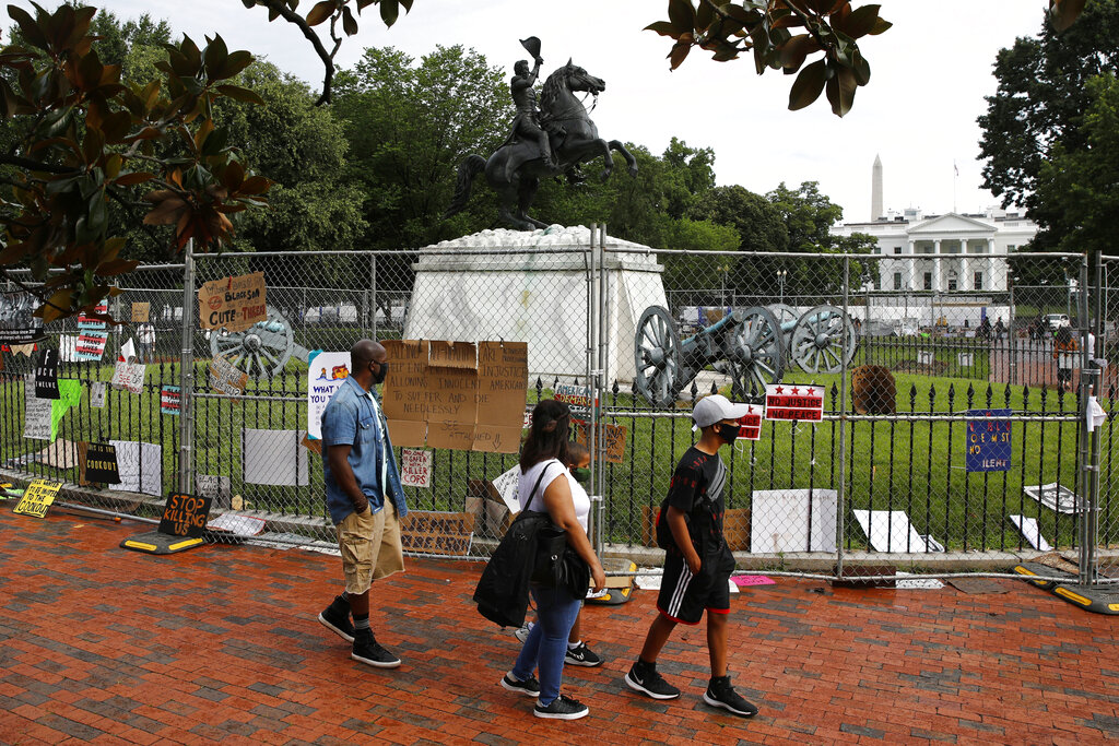 People wear face masks to protect against the spread of the new coronavirus as they walk past protest signs affixed to fencing surrounding a statue of President Andrew Jackson in Lafayette Park 