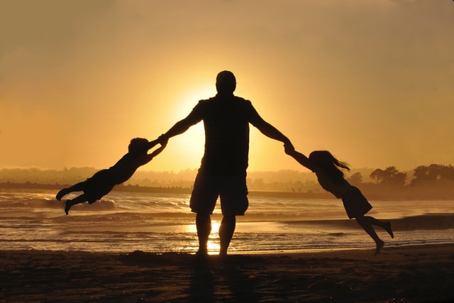 dad swings his daughter and son around on a beach at sunset