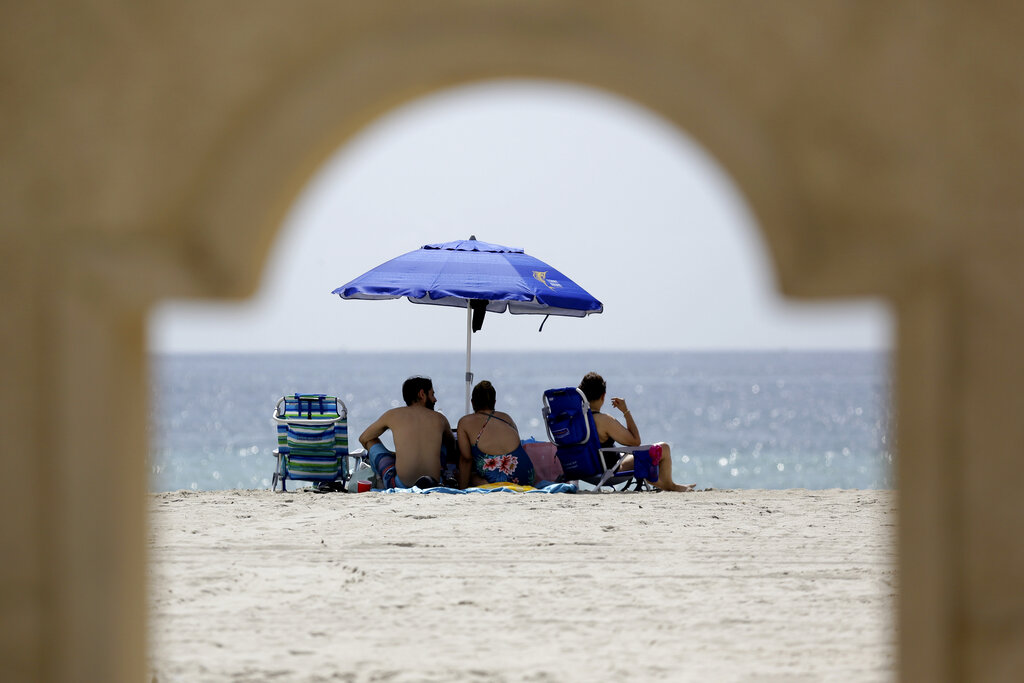 People sit on Hollywood Beach during the new coronavirus pandemic, Thursday, July 2, 2020, in Hollywood, Fla. In hard-hit South Florida, beaches from Palm Beach to Key West will be shut down for the Fourth of July holiday weekend.