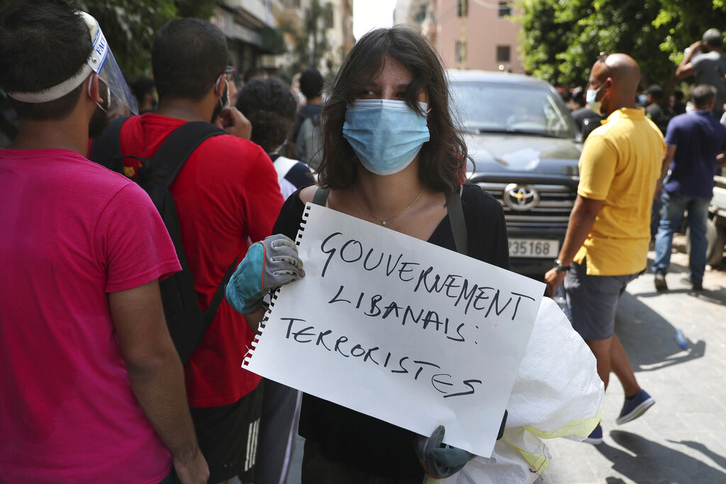 A woman holds a placard in French that reads, "Lebanese government terrorists," next to a convoy of French President Emmanuel Macron 