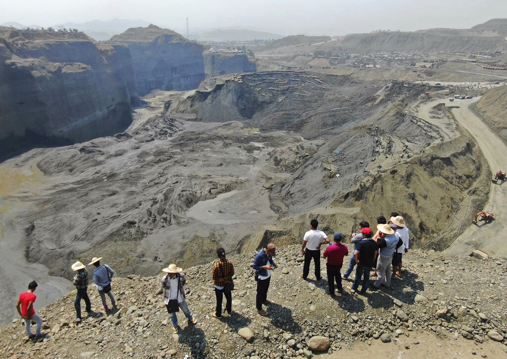 People stand atop a ridge overlooking the scene of a mudslide at a jade gemstone mining site