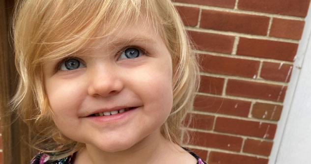 Little blond girl smiling in front of brick wall