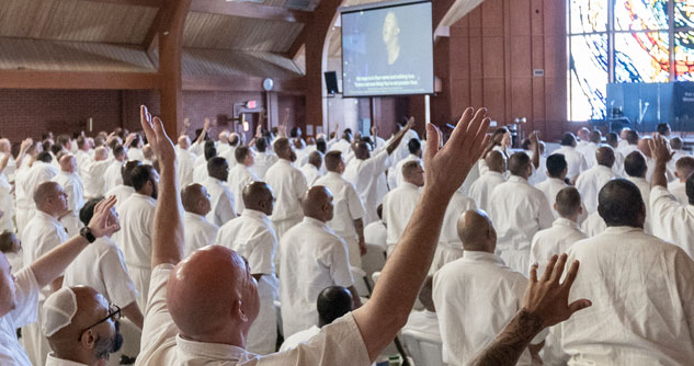 men in white in a chapel, holding up their hands