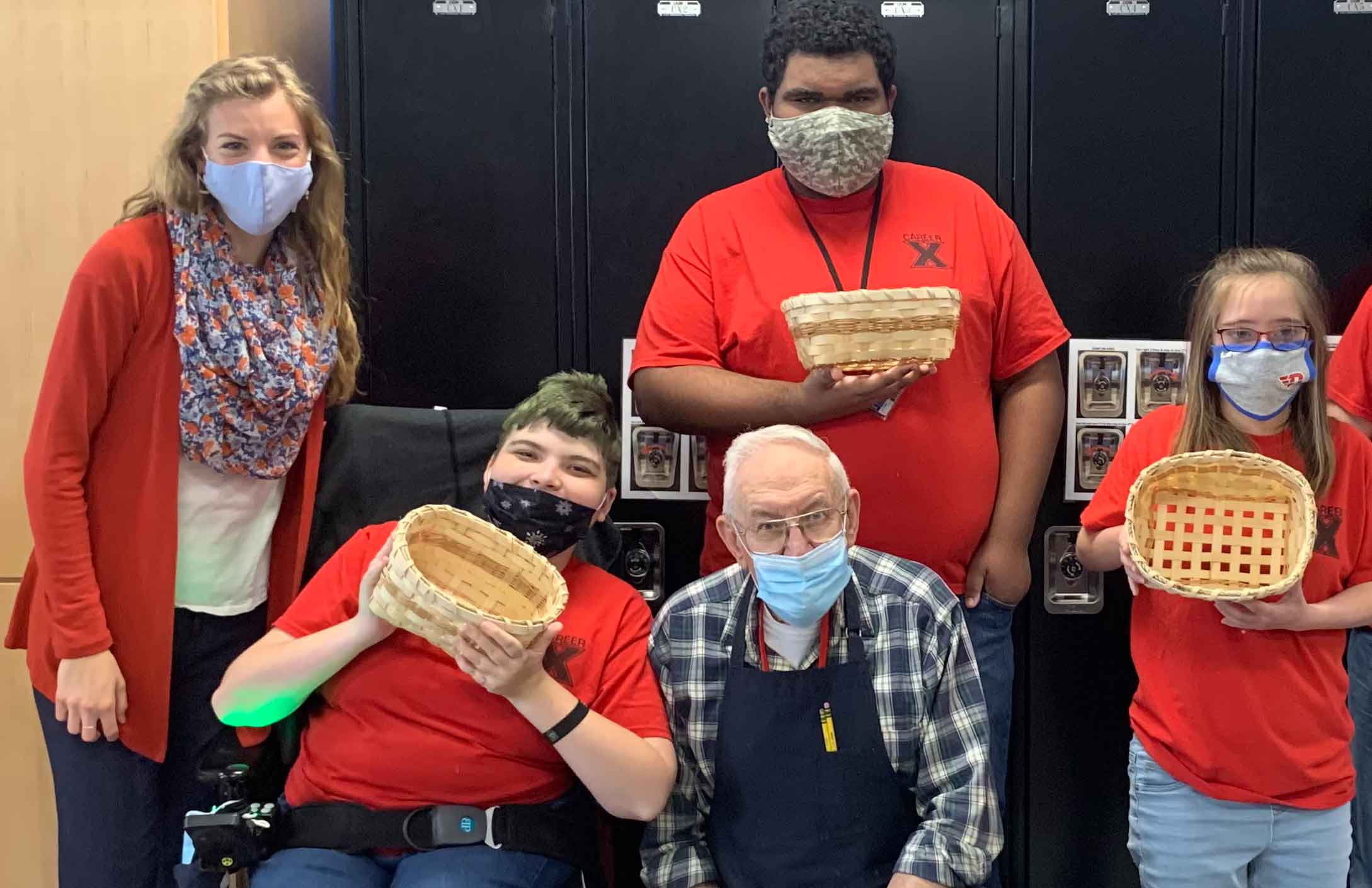 Anna and John smile amongst students who display the baskets they made in John’s basket weaving class. 