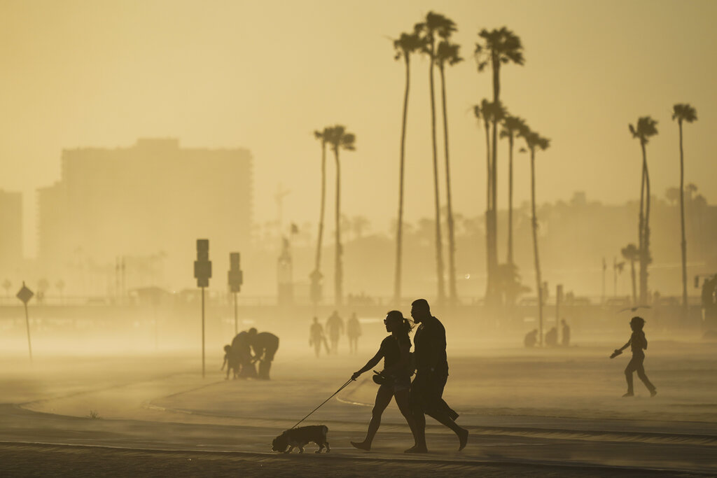 People walk on a beach path as evening winds kick up sand in Long Beach, Calif
