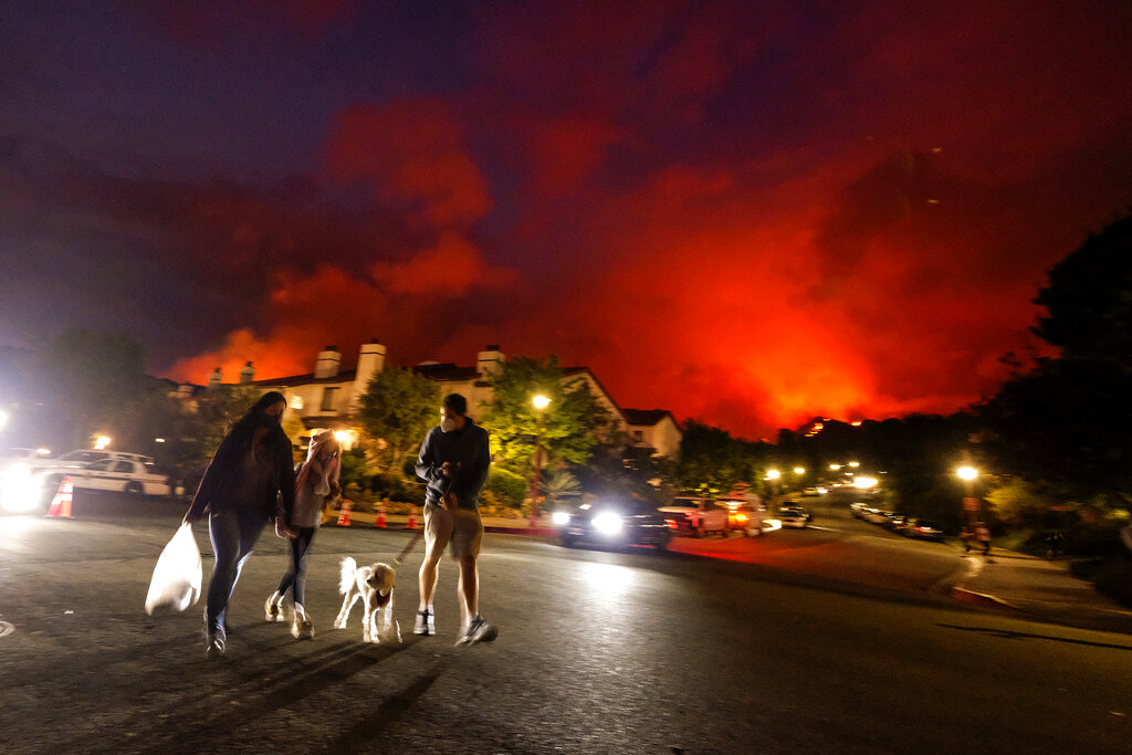 Residents walk a dog as a brush fire burns behind homes in the Pacific Palisades area of Los Angeles