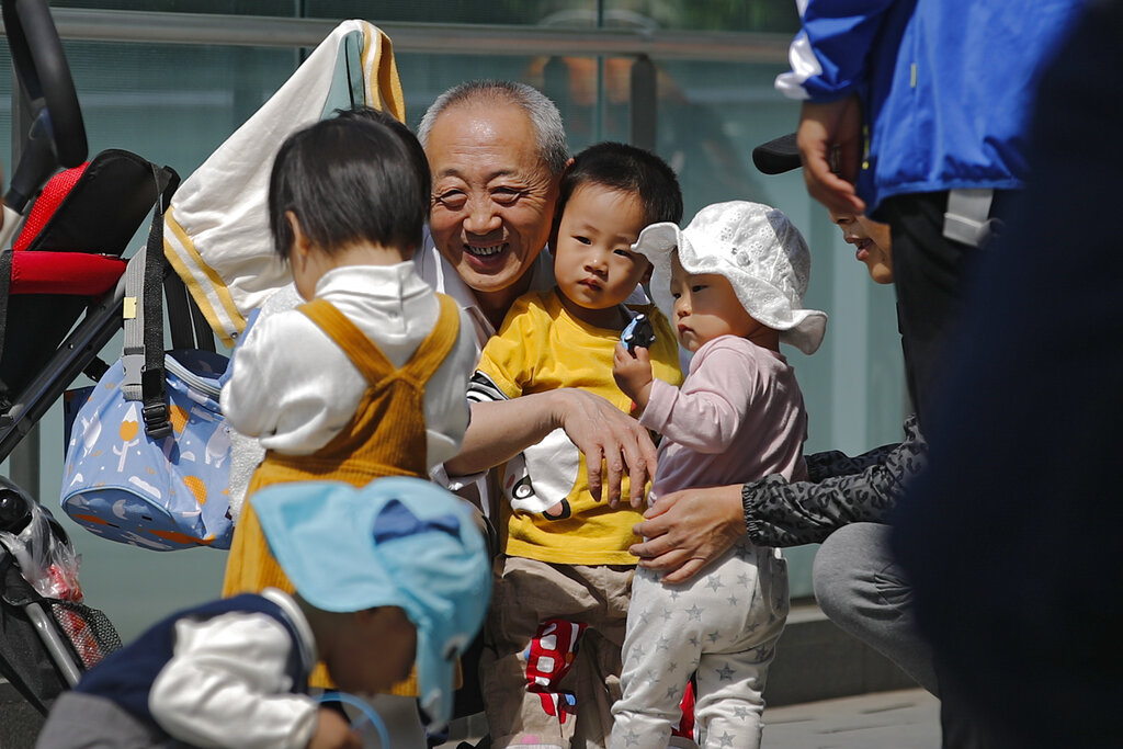 An elderly man plays with children near a commercial office building in Beijing