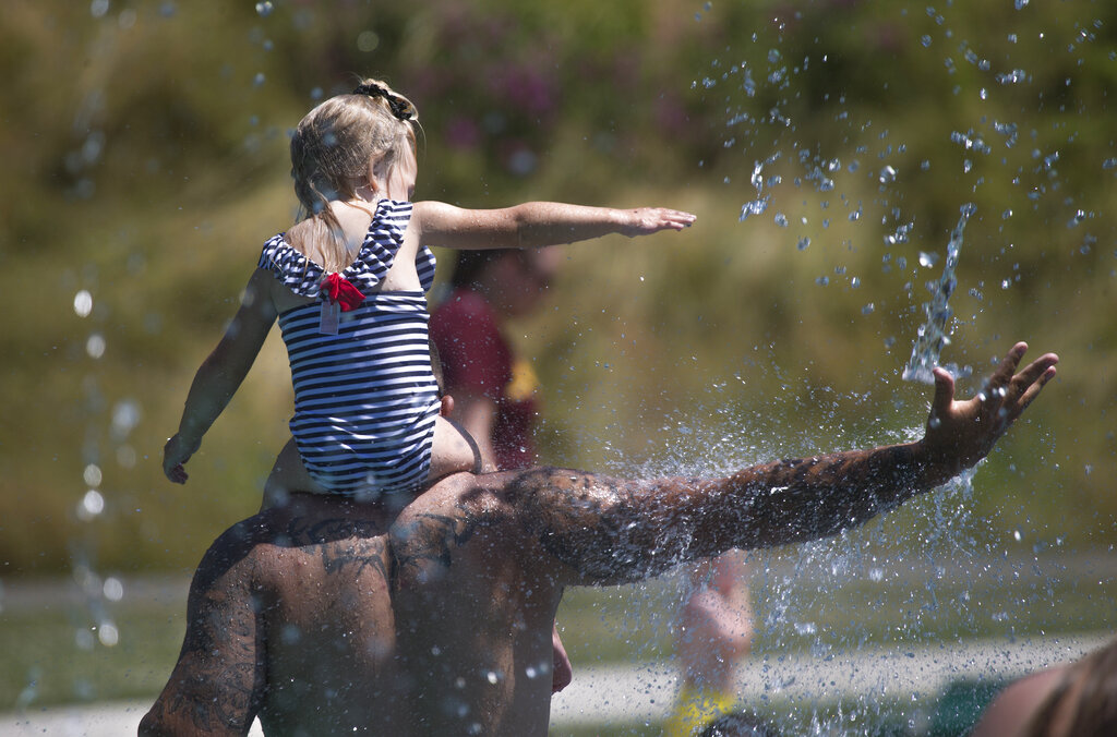 Keeping cool in record setting temperatures, Beau Jess and daughter River, 3, reach for falling water as they play at the Splash Pad in Haller Park on Monday, June 28, 2021 in Arlington, Wash.