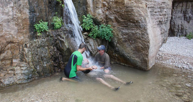 Two men helping a man be baptized under a waterfall