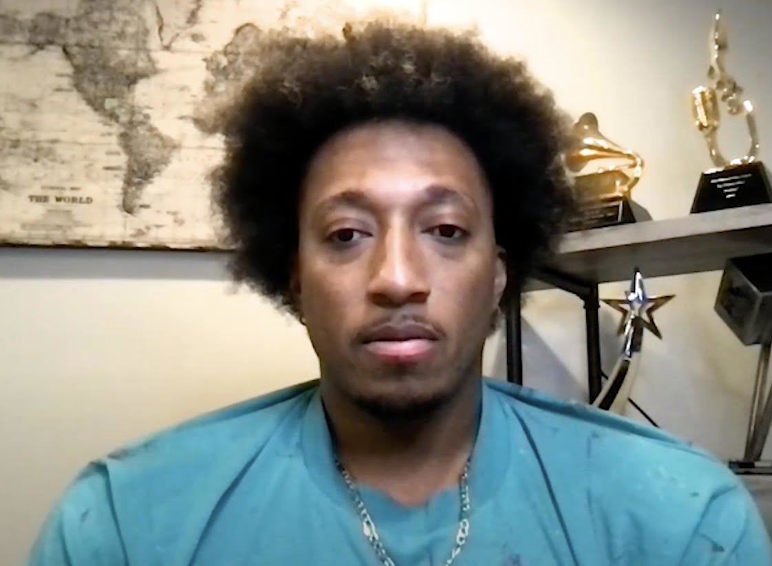 Lecrae with a blue t-shirt on his awards in the background