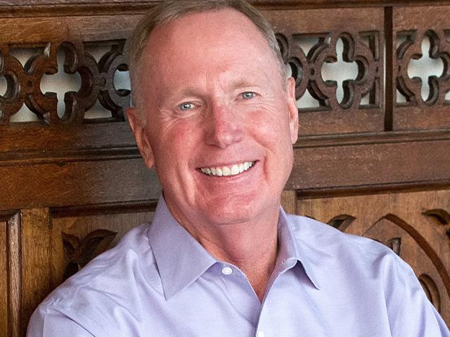 Pastor Max Lucado leaning against a carved wooden bench