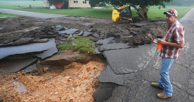 Man looking at severely damaged road with a ruined house in the background