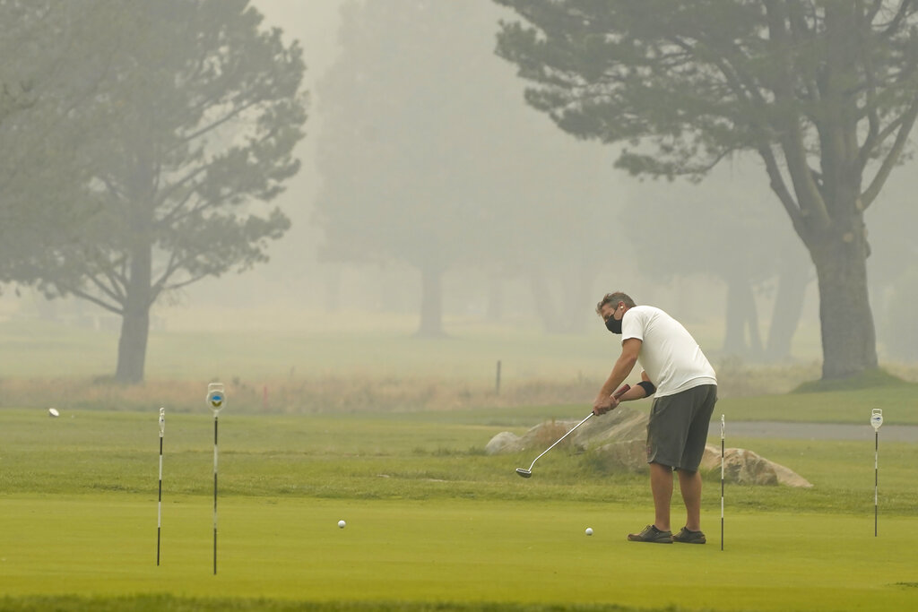 A golfer wears a face mask as he practices his putting at the smoke shrouded Lake Tahoe Golf Course