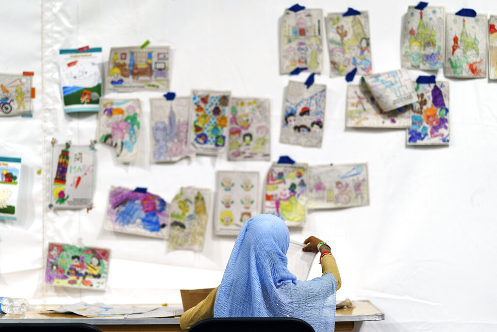 A child holds up a piece of artwork while drawing in a tent at Fort Bliss