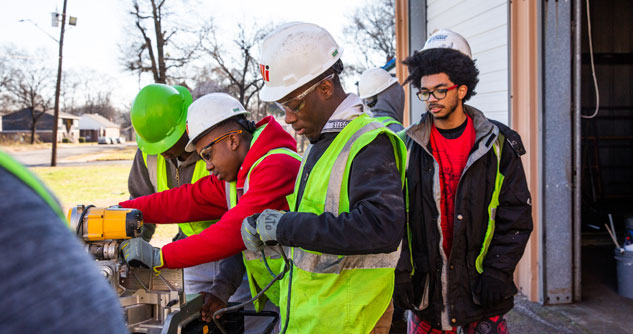 Young people in hard hats and a skill saw