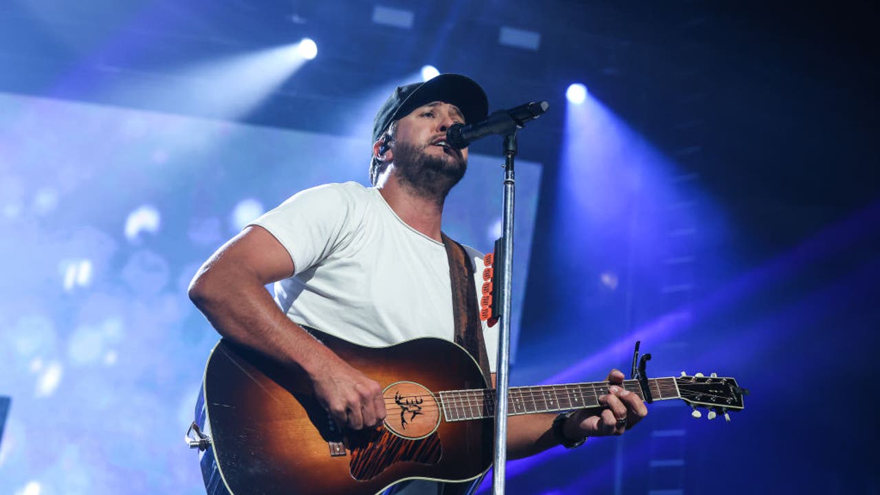Man with white T-shirt singing into a microphone with a guitar in his hands