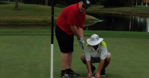 Man holding golf club while volunteer helps