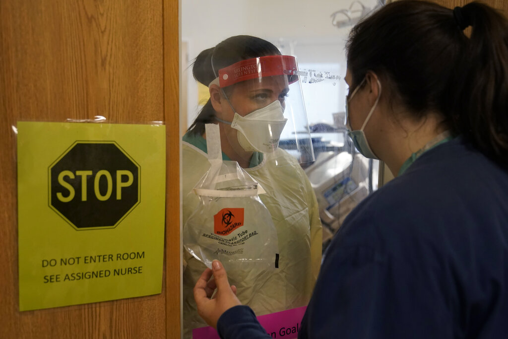 Clinical Nurse Supervisor Melinda Chapin, of Holderness, N.H., left, communicates through glass from inside a COVID-19 isolation room with registered nurse Rachel Chamberlin, of Cornish, N.H., right, at Dartmouth-Hitchcock Medical Center, in Lebanon, N.H.