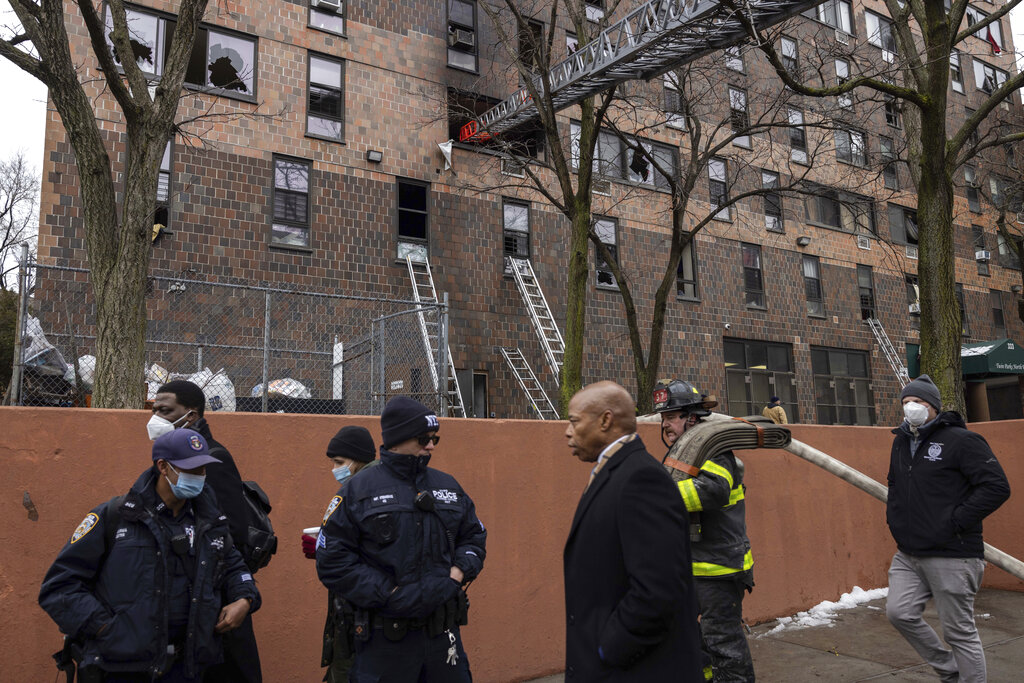 New York City Mayor Eric Adams, third right, walks by an apartment building where a deadly fire occurred in the Bronx