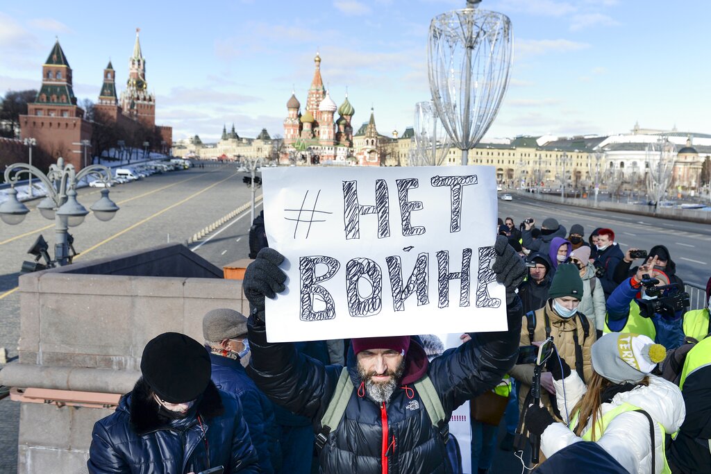 A man holds a poster which reads "No War" as people lay flowers near the place where Russian opposition leader Boris Nemtsov was gunned down, with the Kremlin Wall, left, the Spaskaya Tower, center, and St. Basil
