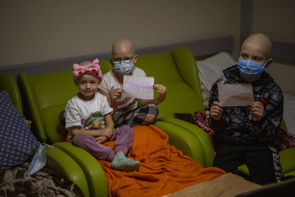 Oncology patients hold up sheets of paper with the words "Stop War" at a basement used as a bomb shelter at the Okhmadet children