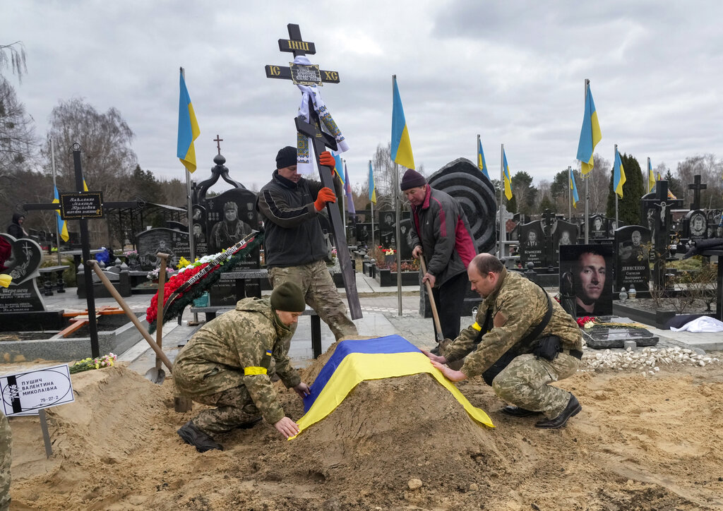 Ukrainian paramedics cover with the National flag the grave of their colleague Valentyna Pushych killed by Russian troops