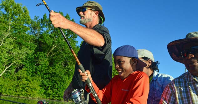 Excited boy holds fishing pole,  assisted by CAD guide while family looks on