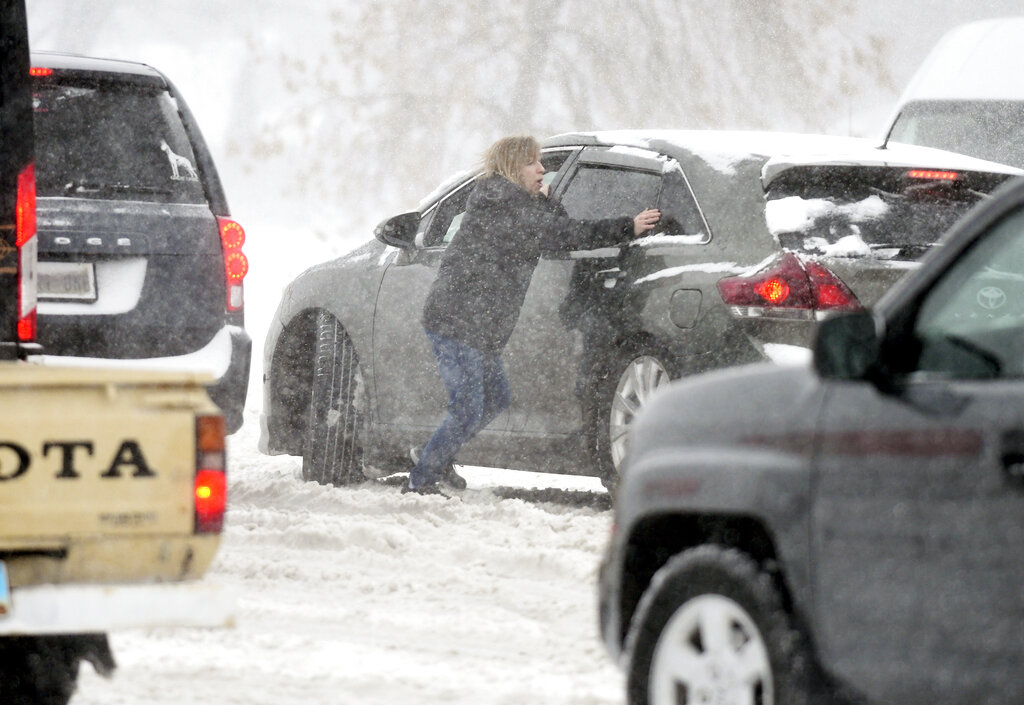 A woman tries to push a stuck car in the snow at the intersection of State Street and Divide Avenue in Bismarck, N.D.