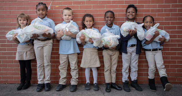 7 schoolchildren in school uniforms holding bags of food